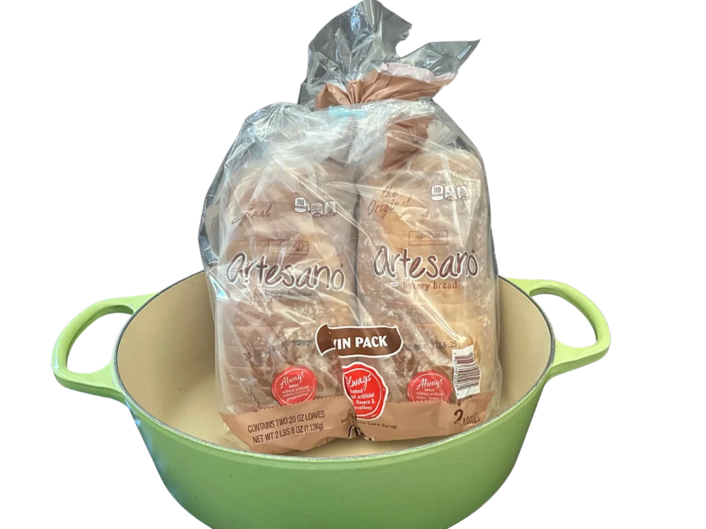 Le Creuset palm colored 9.5 qt oval dutch oven without a lid with two loaves of bread sitting in the pot to show the capacity