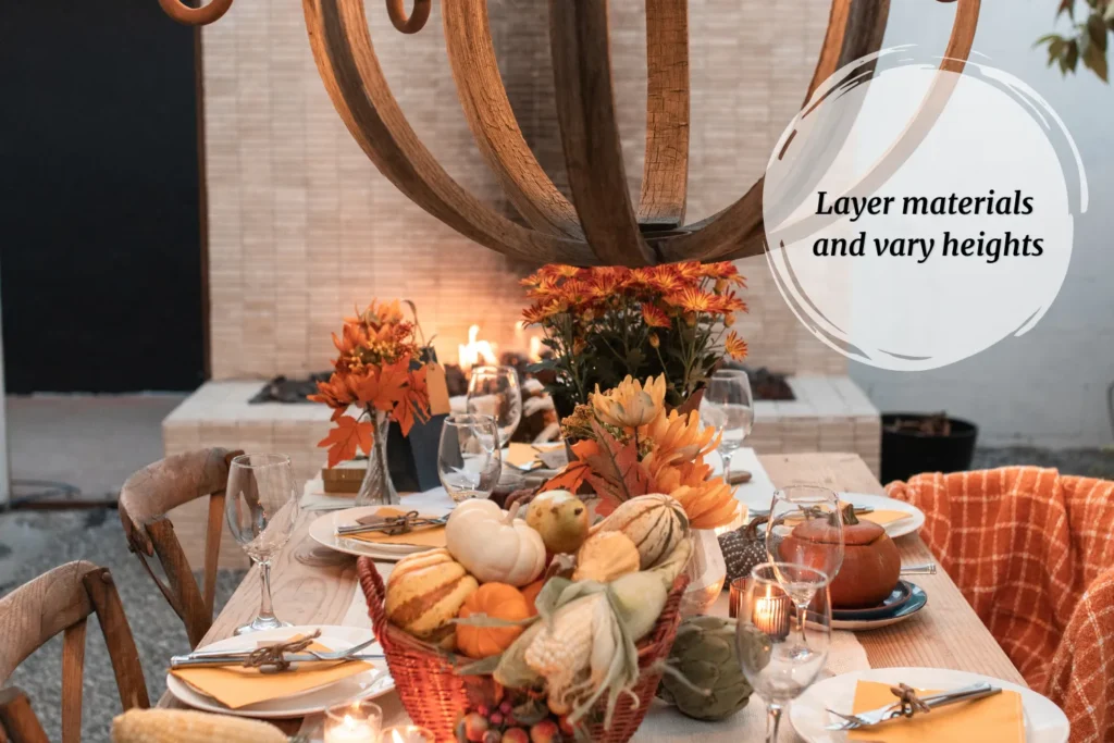 Autumn entertaining tablescape with pumpkins, wood chargers, and Le Creuset cocotte, styled with greenery and layered materials. Text overlay reads Layer materials and vary heights