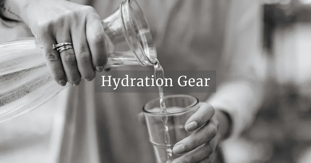 Black-and-white close-up of water being poured from a glass carafe into a drinking glass, section header image for Hydration Gear.