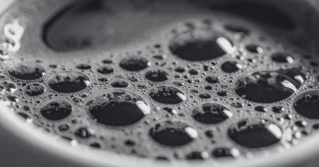 Black and white close-up of coffee surface with bubbles, evoking precision, texture, and engineered clarity