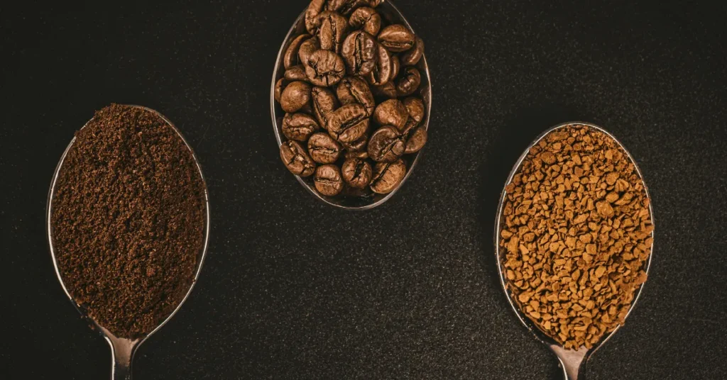 Three metal spoons showing whole beans, ground coffee, and instant granules — evoking grind precision and dose clarity