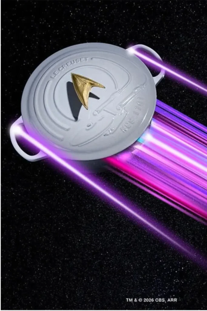 Le Creuset Star Trek collection Enterprise Dutch oven with Starfleet Delta knob against a black space background with purple light trails.